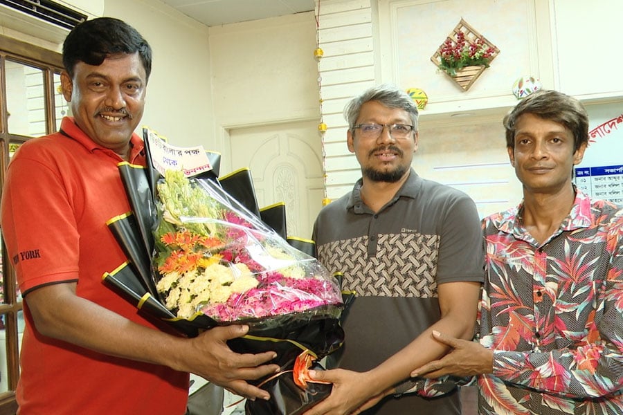 শিবা সানুকে ফুলেল শুভেচ্ছা জানাচ্ছেন ভিওডি বাংলার হেড অব নিউজ রেজাউল করীম হীরা ও প্রধান প্রতিবেদক রুদ্র রাসেল। ছবি: ভিওডি বাংলা
